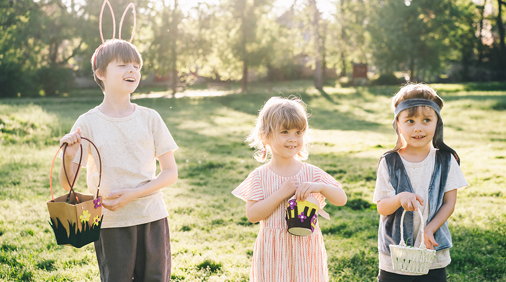 Three children in sunlight wearing bunny ears and holding easter baskets